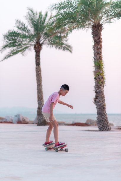 亚洲男孩愉快地在海滩滑冰在晚上。图片下载