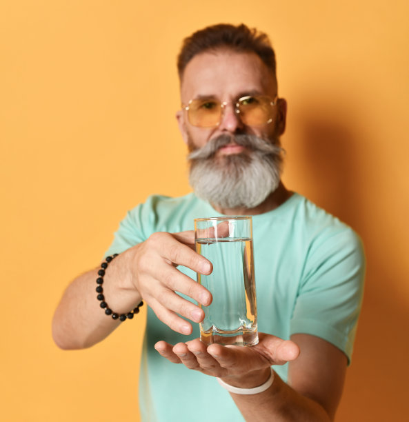 一个胡子男子的手捧着一杯水，靠在一堵橙色的墙上图片下载