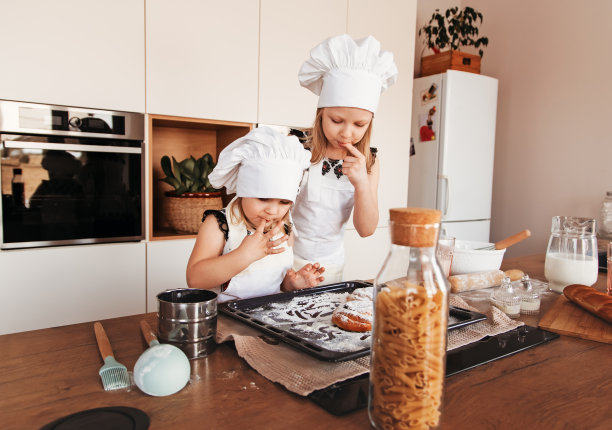 小女孩们戴着白色厨师帽在厨房品尝糕点图片下载