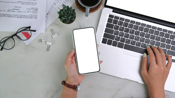 头顶上的照片，一位女商人拿着手机，在大理石桌子上用笔记本电脑工作。图片下载