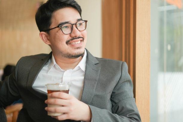 近距离观察成年中东商人透过办公室的窗户看外面，微笑着思考新想法，拿着冰咖啡杯的未来商业理念的愿景图片下载