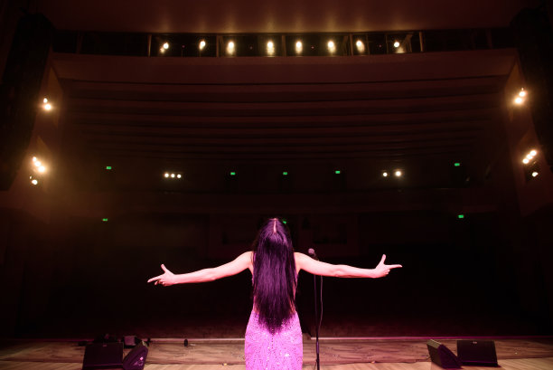 美丽的歌手在礼堂里。后视图女孩在舞台上表演长礼服。图片下载
