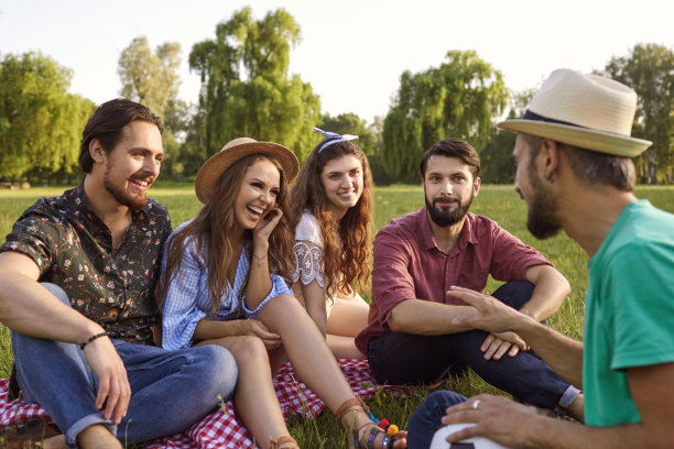 一群年轻人在夏日公园的草地上野餐，谈笑风生。图片下载