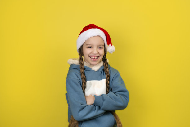 十几岁美丽的女孩在圣诞老人的帽子长辫子微笑孤立在黄色背景。图片下载