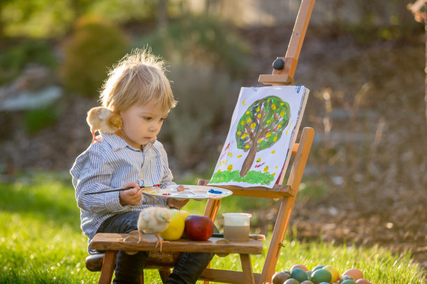 可爱的蹒跚学步的孩子，在花园里画鸡蛋，小鸡在他周围跑图片下载