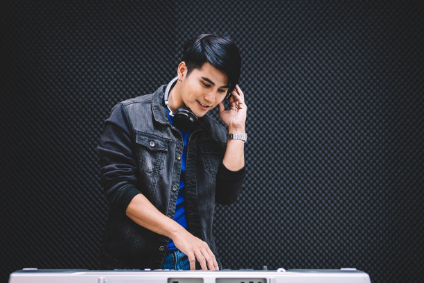亚洲男性在录音棚里戴着耳机弹奏电子键盘。使用带有拷贝空间的录音棚麦克风录制歌曲。图片下载