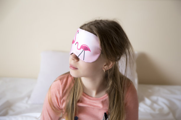 漂亮的年轻褐发女孩穿着粉色睡衣，眼睛上戴着睡眠面罩。女孩早上醒来，概念快乐开始新的一天图片下载