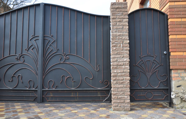 这是对房子附近一扇黑色金属锻造铁门和钢栅栏的特写。铁艺栅栏装饰品。图片下载