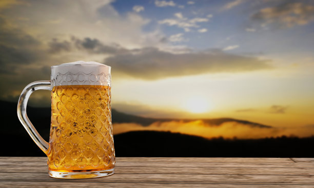 清澈的啤酒杯，杯口有冰啤酒和泡沫，杯口有水滴附着。木板或木板表面，并与山风景在早晨的阳光。三维渲染图片下载
