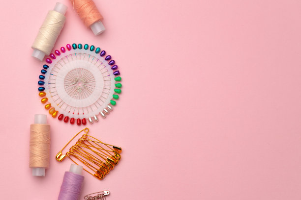 缝纫配件，包括线轴和粉红色背景上的大头针图片下载