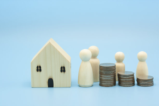 一个木制的房子，木制的玩偶和硬币堆的钱显示概念家，贷款，财产，未来计划，保险和复制空间旗帜。图片下载