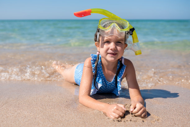 可爱的女孩穿着蓝色泳衣，戴着潜水面罩躺着
在沙滩上。孩子准备好潜水了。快乐的孩子戴着护目镜和通气管在暑假图片下载