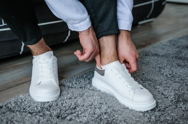 那家伙正在系白色运动鞋的鞋带。新郎穿着漂亮的运动鞋，系着鞋带。图片下载