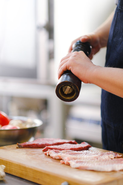 厨师给一块肉加了盐和胡椒。在餐厅的厨房里做饭。图片下载
