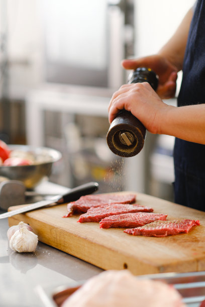 厨师在一块肉上撒上盐和胡椒。在餐厅的厨房做饭。图片下载