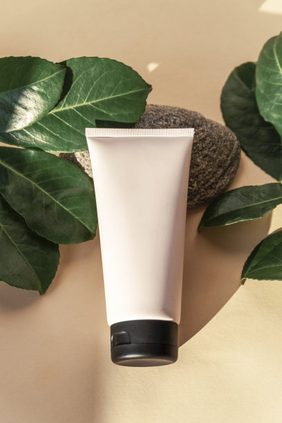 奶油管在天然石材上与绿色叶子在中性背景，俯视图，平铺。模拟了图片下载