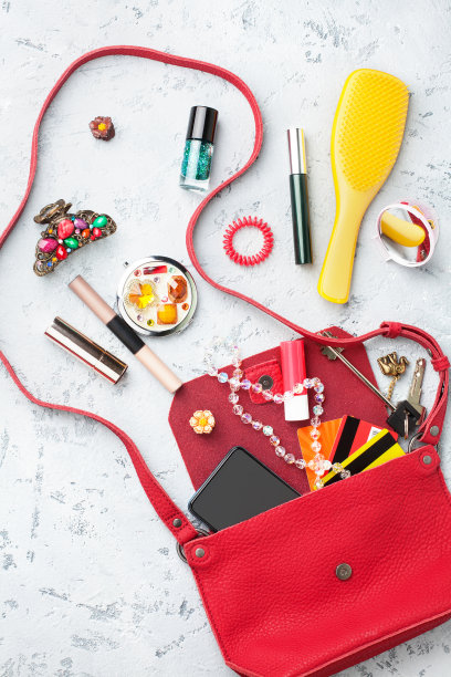 打开红色皮质女式手袋，灰色背景近观俯视图，化妆化妆品，发刷，发夹，智能手机，家钥匙，信用卡，女性时尚概念，女孩的手袋配件，平躺图片下载