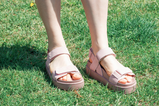 在绿草的背景下，穿着夏日凉鞋的女脚丫。图片下载