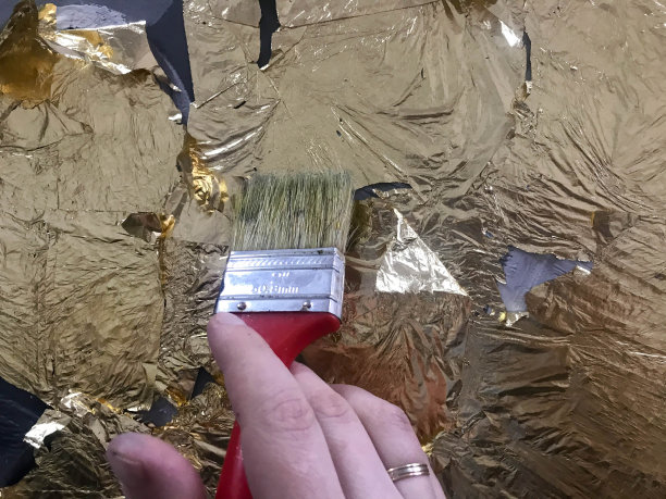 艺术家的手用画笔绘画，用金箔闪闪发亮的亮黄色金属金箔在画布上进行艺术创作。背景图片下载