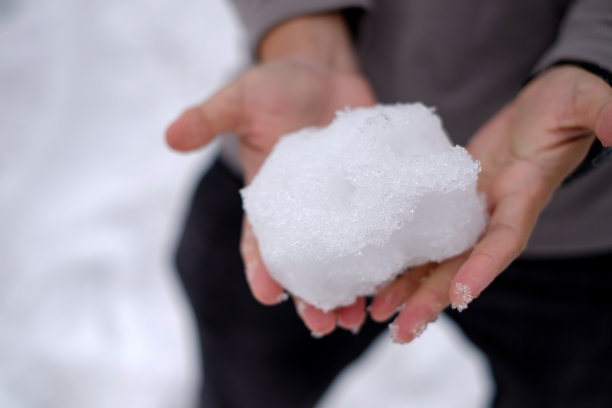 男子双手捧着一场雪白的雪，他试图捧着雪，却没有戴手套，所以在雪的背景下旅行期间很冷。图片下载