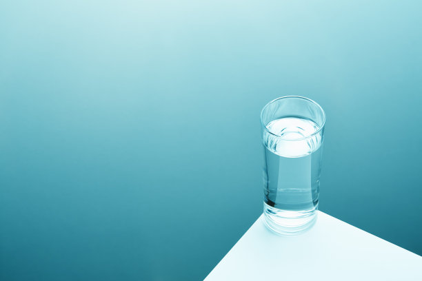 白色桌子的边缘放着一杯清澈的饮用水，背景是柔和的渐变图片下载
