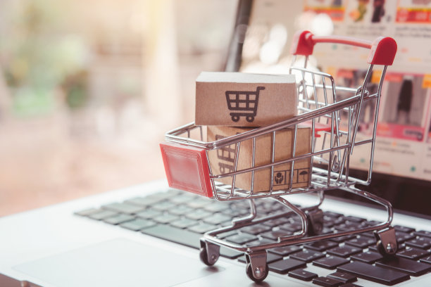 在线购物。在笔记本电脑键盘上的手推车上有一个带有购物车标志的纸板箱。网上购物服务。提供送货上门图片下载