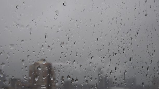 湿漉漉的窗玻璃上滴着水滴，模糊了窗后的城市风景图片下载