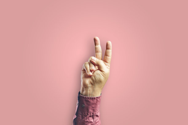 手臂做胜利的手势，手孤立在粉红色的背景。图片下载