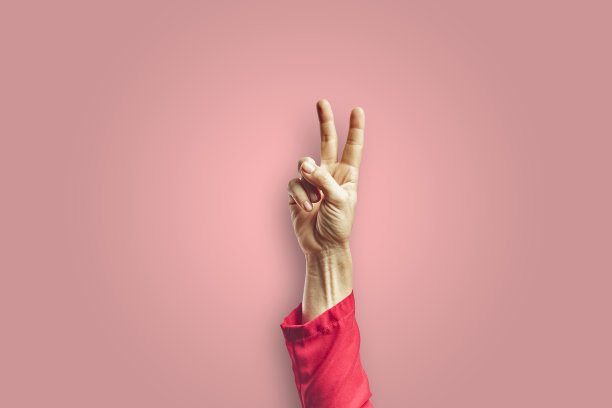 女人的手臂做出胜利的手势，手孤立在粉红色的背景上。图片下载