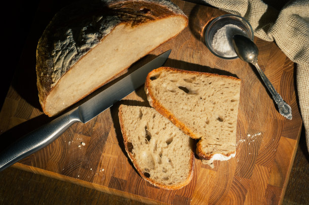 静物-无酵母荞麦面包片，粗盐在一个玻璃罐里，一把刀，亚麻餐巾在一块木板上，一个木制的背景，硬光，一张低调的照片。图片下载