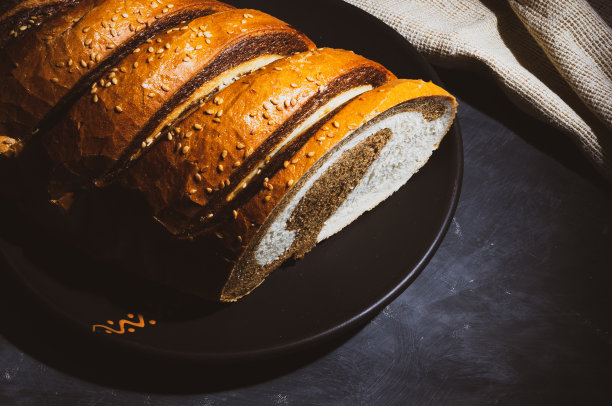 不寻常的两种颜色的新鲜面包在陶瓷盘子和编织餐巾在黑色的背景，照片在一个低的关键，强光，特写。图片下载