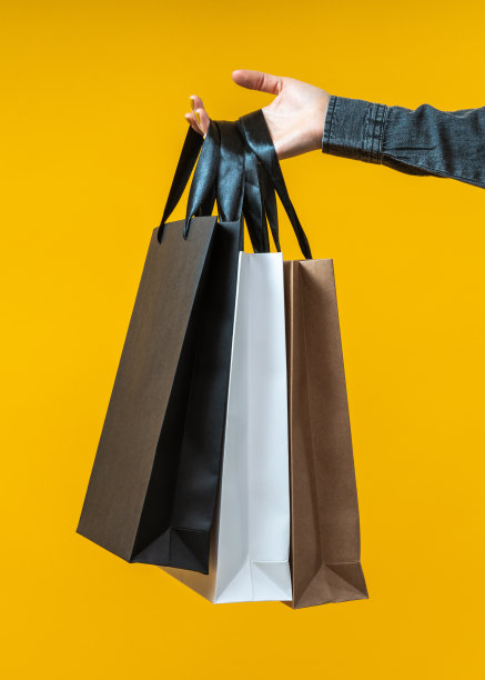 垂直拍摄的女性手握一群购物者的白色，黑色和牛皮纸，孤立在明亮的黄色背景图片下载