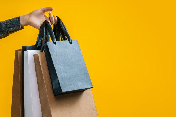 工作室拍摄的女性手握一群购物者的白色，黑色和牛皮纸，孤立在明亮的黄色背景图片下载