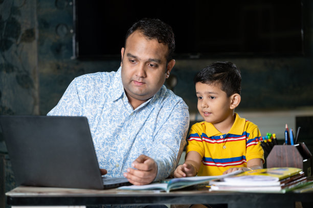 快乐的父亲在家里用笔记本电脑和智能手机帮助儿子学习。图片下载