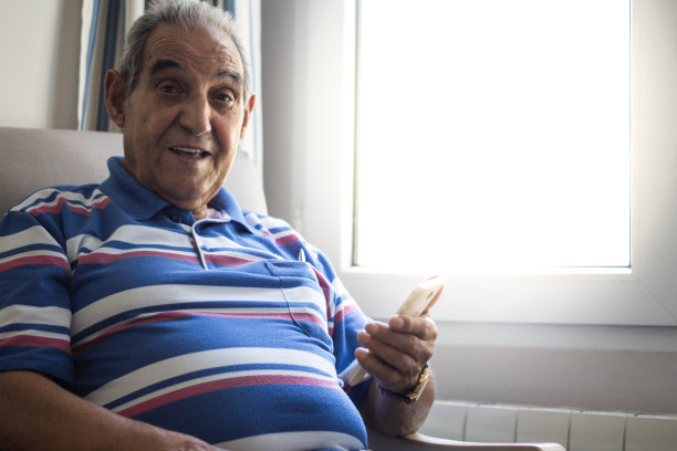 一位高管坐在扶手椅上，微笑着拿着智能手机，身穿条纹polo衫，靠窗而立图片下载