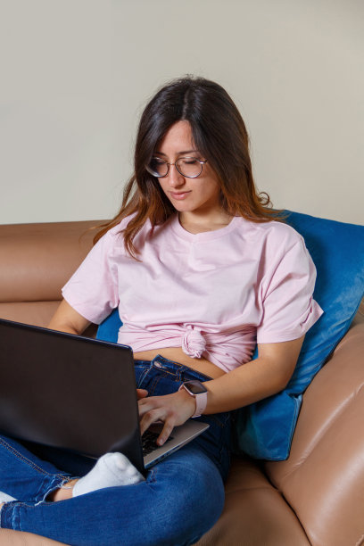 年轻女性坐在家里的沙发上用笔记本电脑工作图片下载