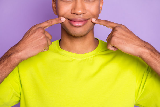 裁剪照片的年轻英俊，有吸引力的快乐微笑的非洲男子手指在嘴唇孤立的紫色背景图片下载