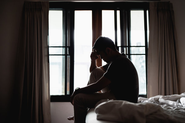 剪影抑郁的男人悲伤地坐在卧室的床上，抑郁的概念图片下载