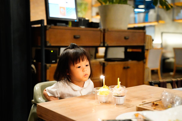 亚洲婴儿吹她的生日蜡烛在餐厅的纸杯蛋糕庆祝她的生日派对。图片下载