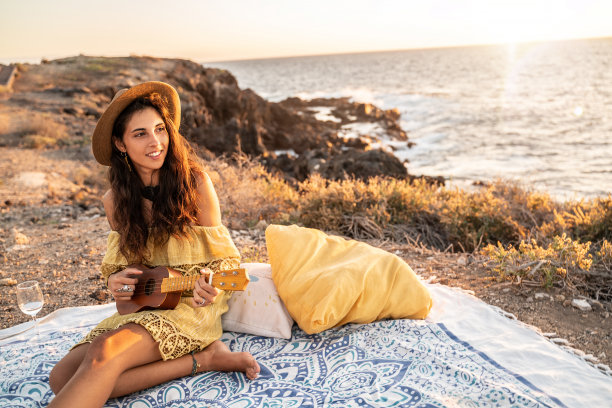 生活方式年轻的波西米亚女子放松在夏天的海滩上，弹着小吉他。图片下载