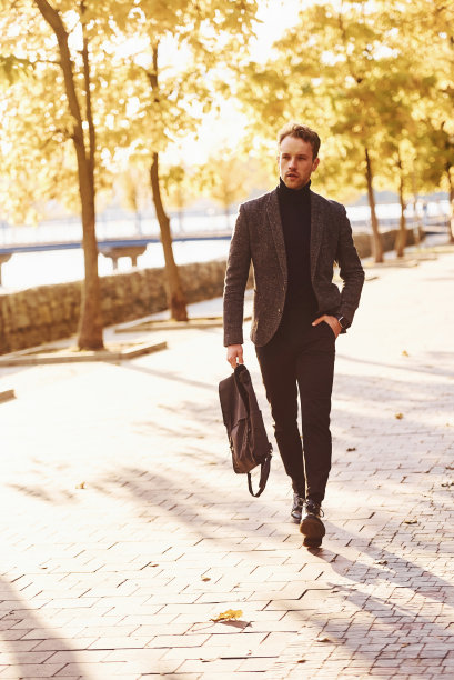 一个年轻人穿着正装在阳光明媚的秋天公园里散步图片下载