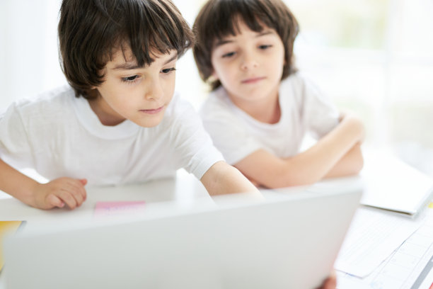 教育孩子。可爱的拉丁男孩看起来很专注，和他的兄弟坐在桌子旁，看着笔记本电脑的屏幕。两个小孩在家上在线课程图片下载