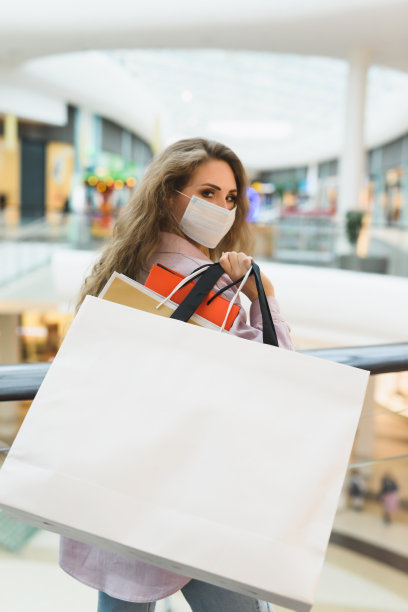 一个年轻的女人戴着医用口罩，拿着从商场不同商店买的很多购物袋。冠状病毒新冠肺炎大流行和封锁。近距离的照片。图片下载