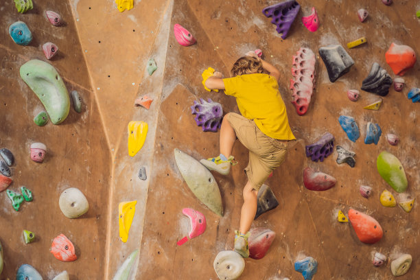 小男孩穿着特制的靴子在爬岩壁。室内图片下载