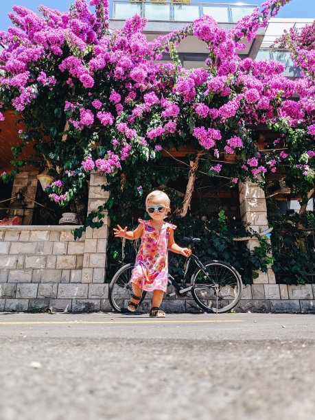 一个小女孩在马路上跑步的时尚照片。在盛开的九重葛树的背景下，一个穿着花背心的孩子。图片下载