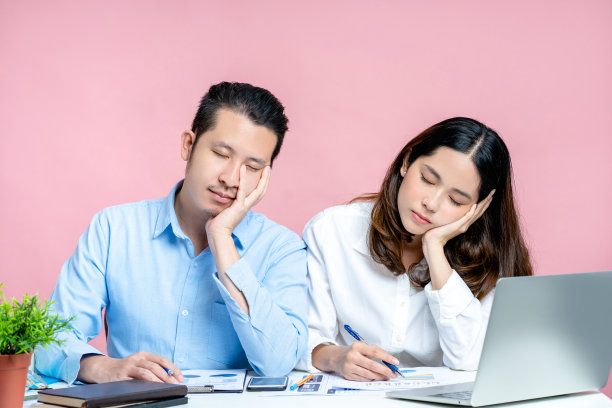 一名疲惫的上班族坐在粉红色背景的办公桌前。他们在办公室里睡着了。过度工作的概念。图片下载