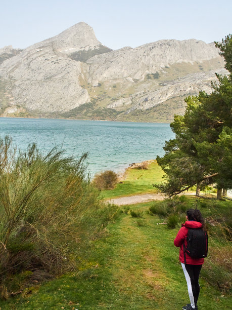 图片右下角的女人穿着红黑相间的衣服，在乡村里，看着欧罗巴山的山脉和湖泊图片下载