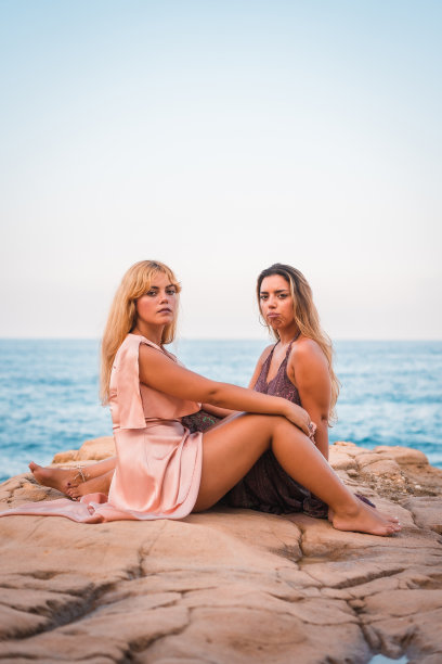 一对白人女孩穿着漂亮的衣服坐在海边享受夏天，垂直照片图片下载
