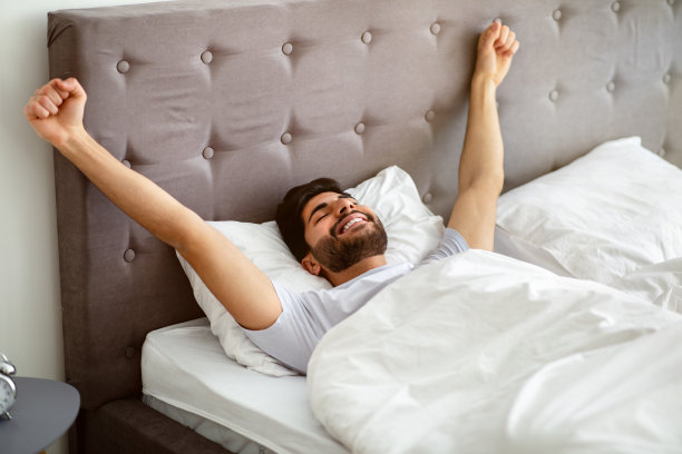 阿拉伯男子在舒适的床上醒来伸懒腰，闭着眼睛图片下载