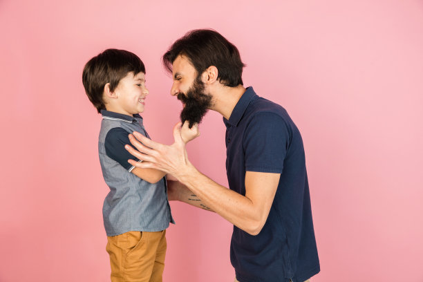 快乐的男人和小男孩，父亲和儿子隔离在粉红色的背景下。图片下载